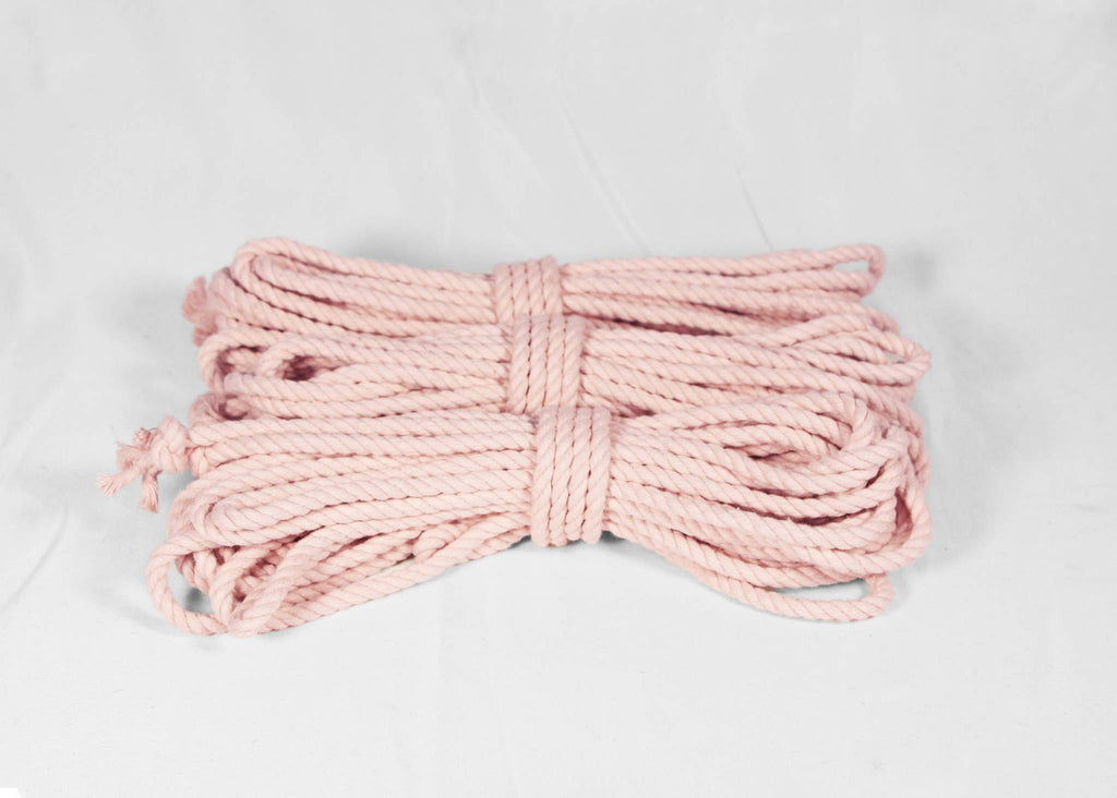 A coiled bundle of light pink cotton rope or cord, tied in the center, displayed on a white fabric background.